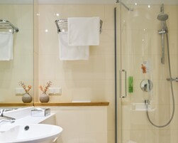 Uma casa de banho moderna com cabine de duche em vidro, lavatório branco e espelho.