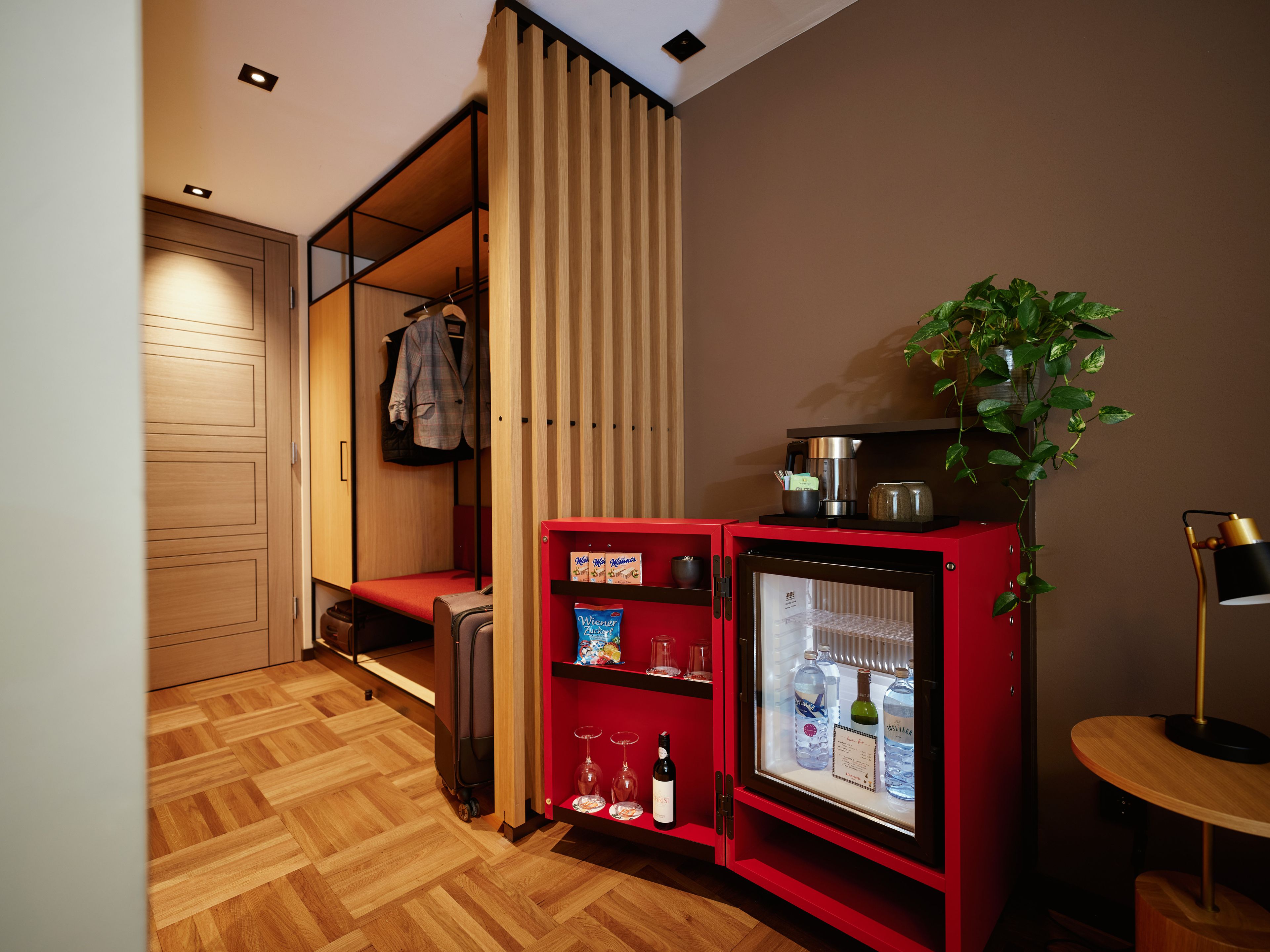 Een compacte kamer met een kitchenette, een zithoek en een klein tafeltje met een lamp.