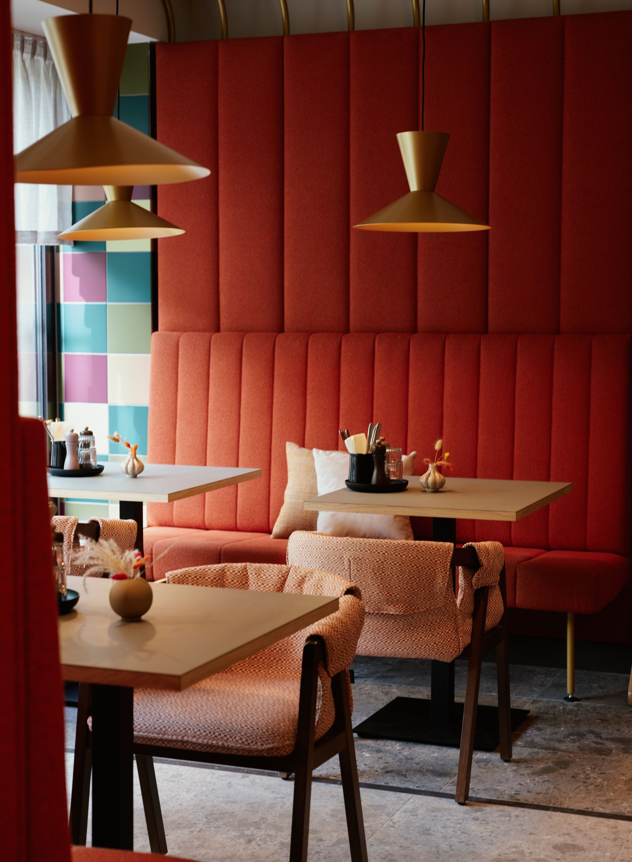 A modern interior with a red padded wall, wooden furniture, and pendant lighting.