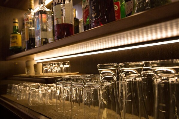 A bar area with shelves of liquor bottles and a row of empty glasses. - Hotel Terminus & Plaza (Pisa)