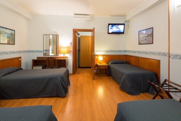 A hotel room with two single beds, a desk with a chair, a TV mounted on the wall, and a door leading to another room.
