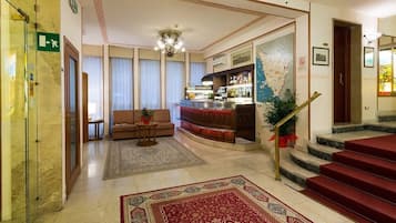 A hotel lobby with a bar, a sofa, a staircase, and a carpeted floor.