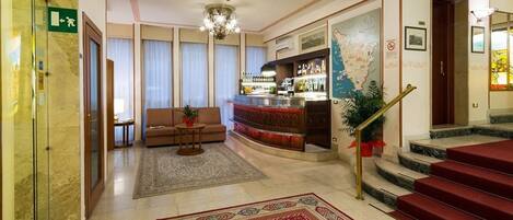 Un hall de hotel con bar, sofá, escalera y suelo alfombrado.