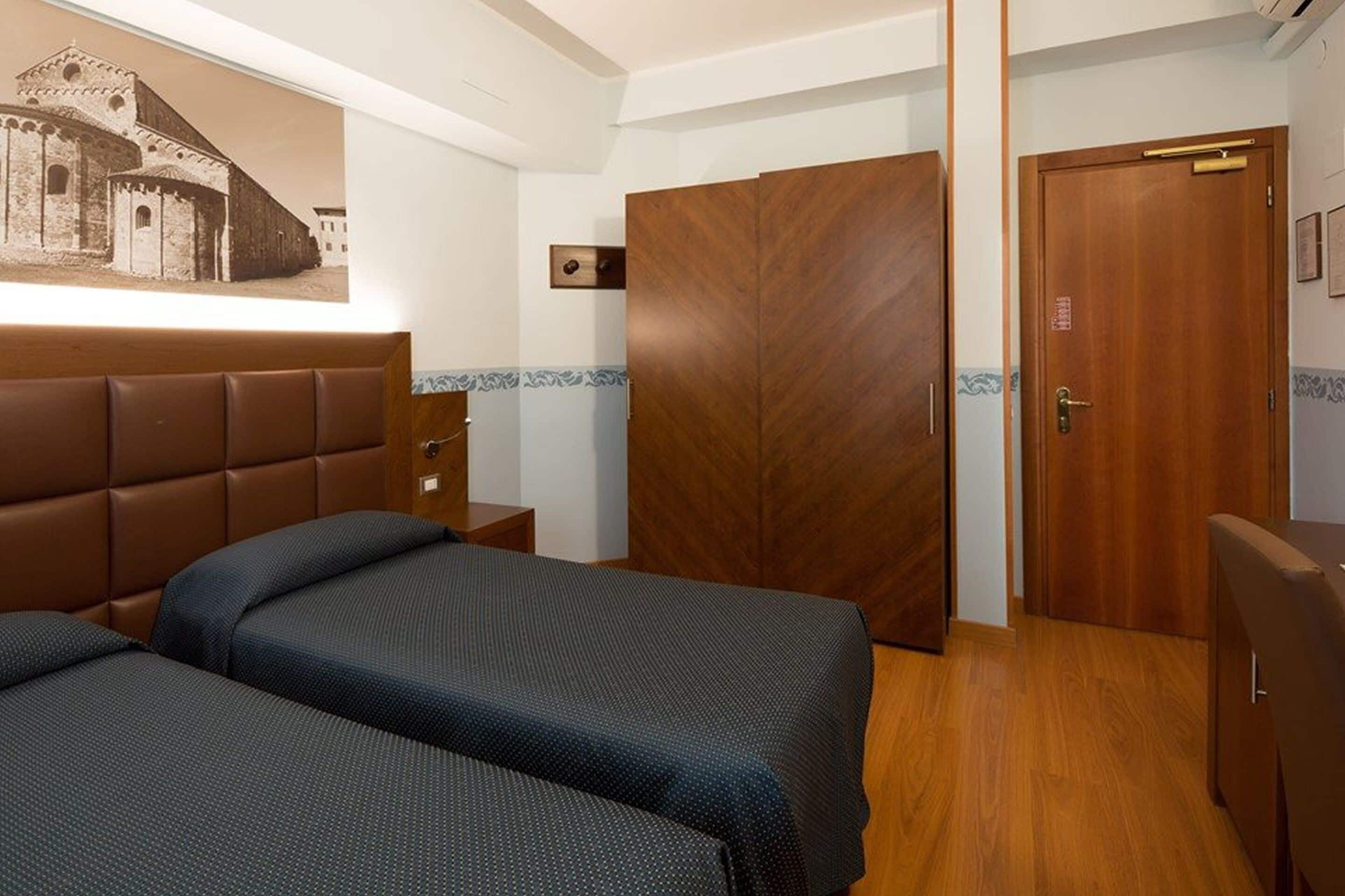 A hotel room with a large bed, a wooden wardrobe, and a door with a handle.