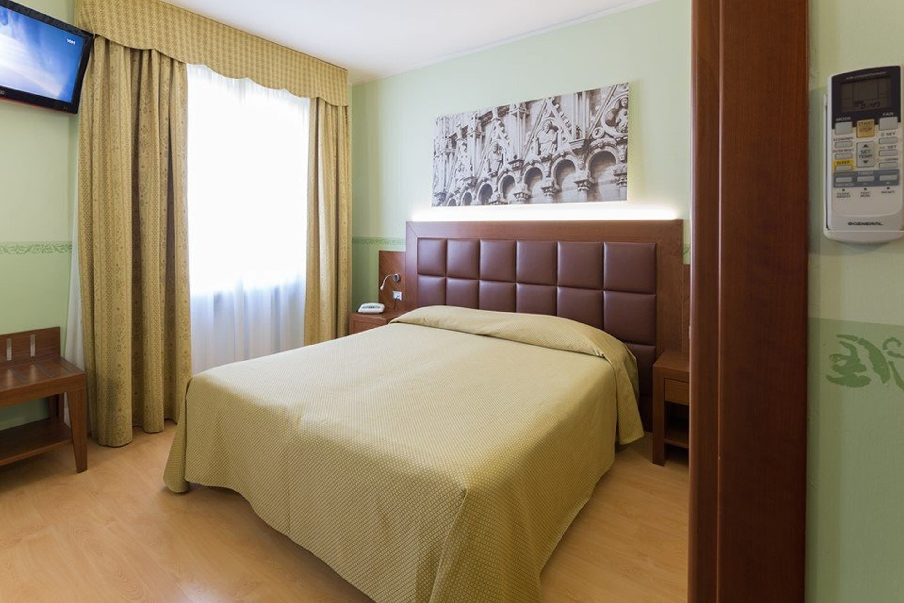 Una habitación de hotel con una cama, un banco, un televisor y un termostato en la pared.