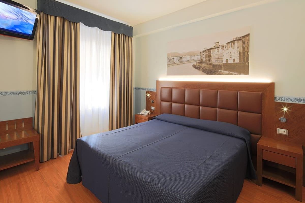Ein Hotelzimmer mit einem großen Bett, einer Holzbank, einem Nachttisch mit Lampe, einem Flachbildfernseher und einem Wandbild.