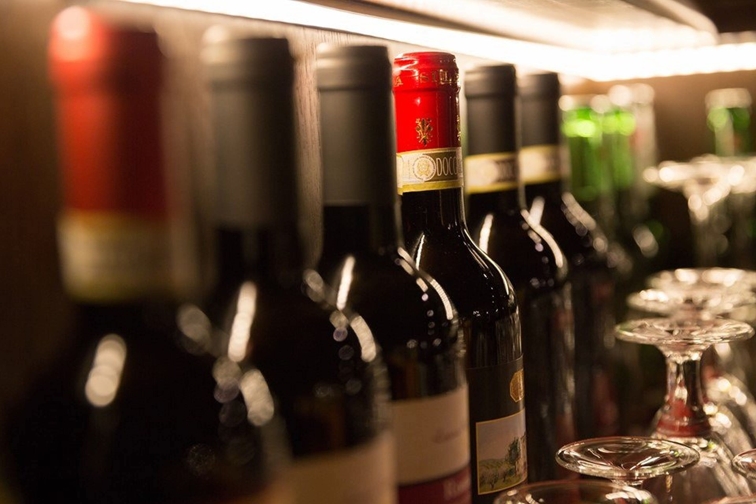 Une rangée de bouteilles de vin, avec leurs étiquettes, et des verres, sur une étagère.