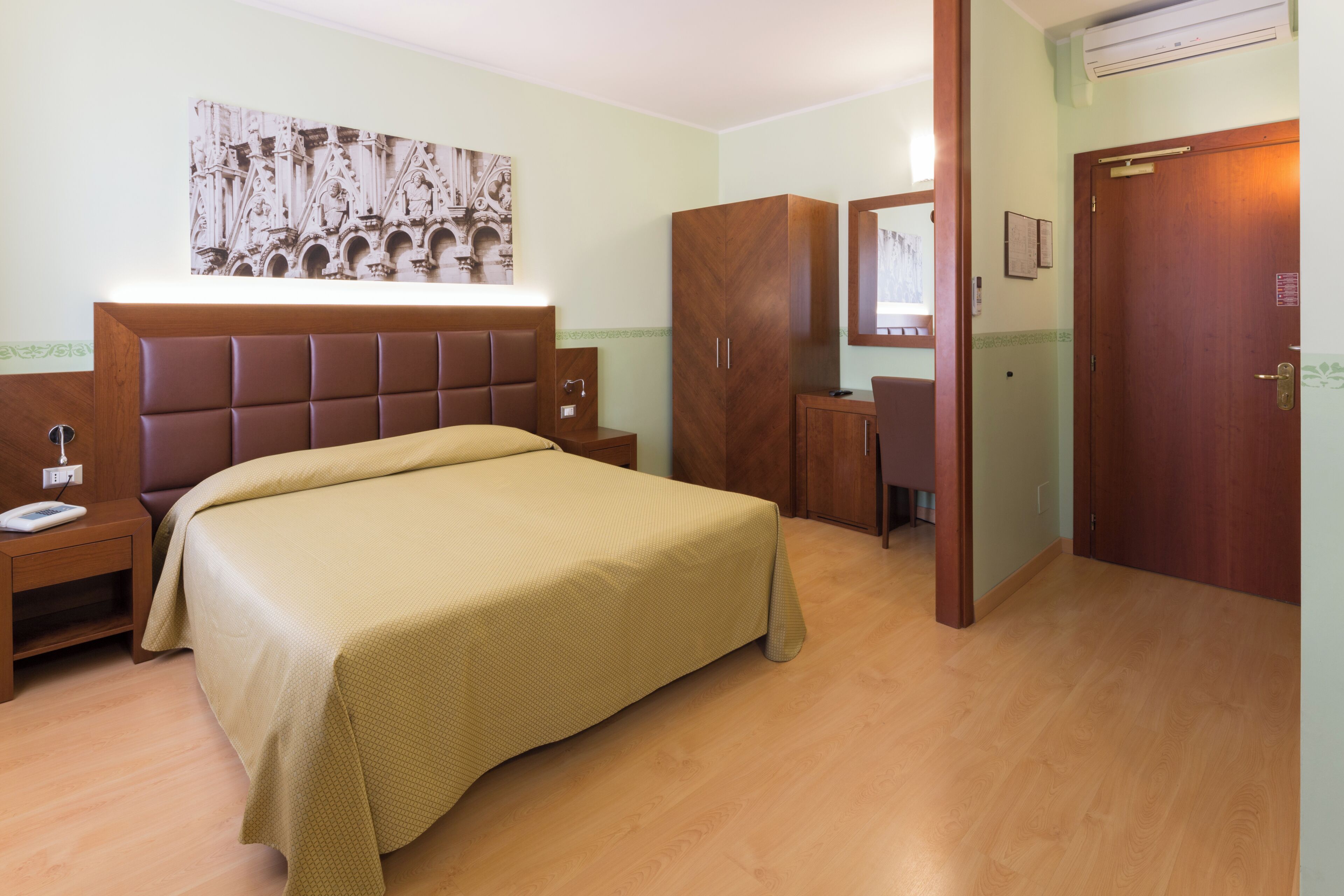 A hotel room with a bed, a wardrobe, a desk, and a mirror.