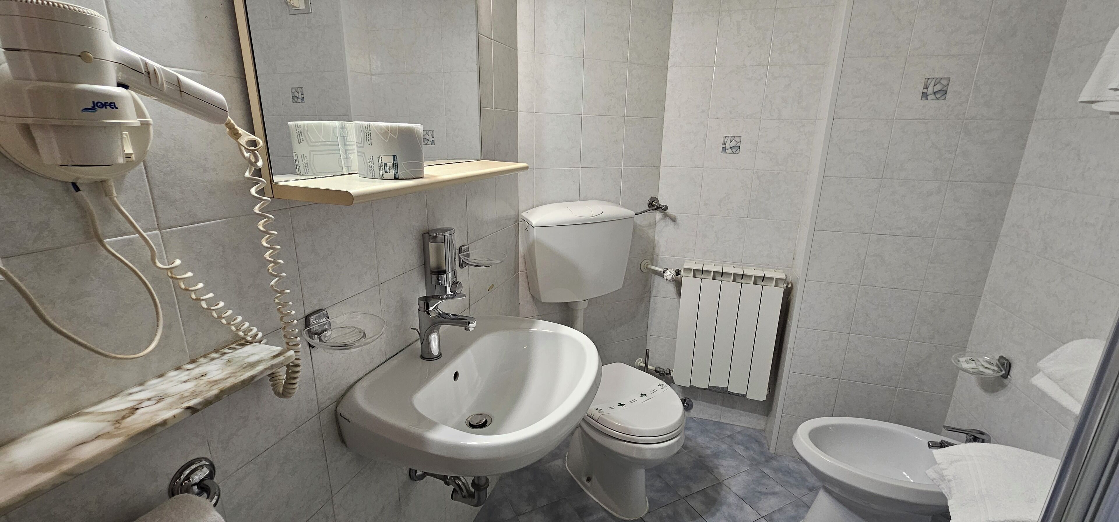 A bathroom with a sink, toilet, bidet, and hairdryer.