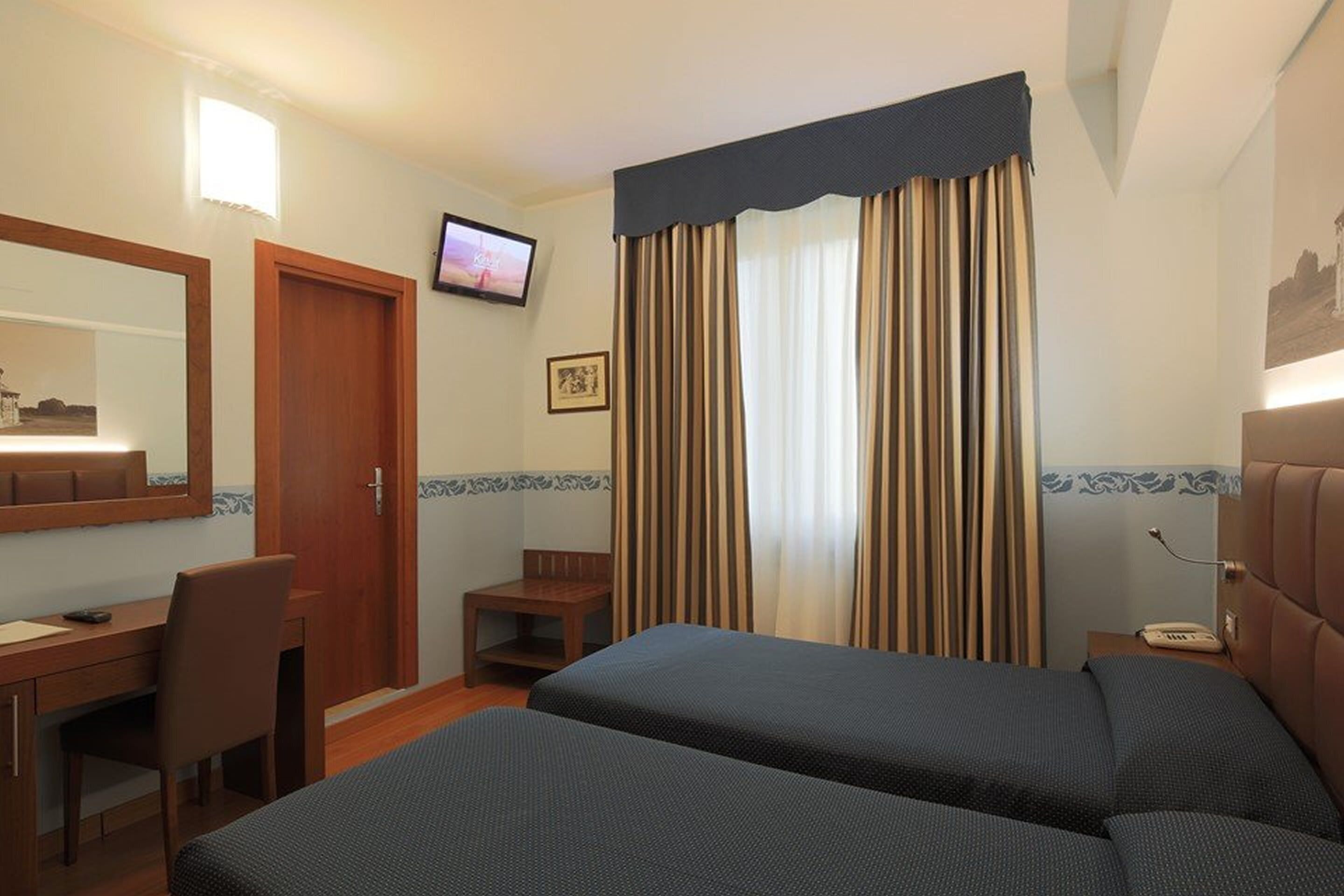 Une chambre d’hôtel équipée d’un lit, d’un bureau, d’une chaise, d’une télévision et d’une fenêtre avec des rideaux.