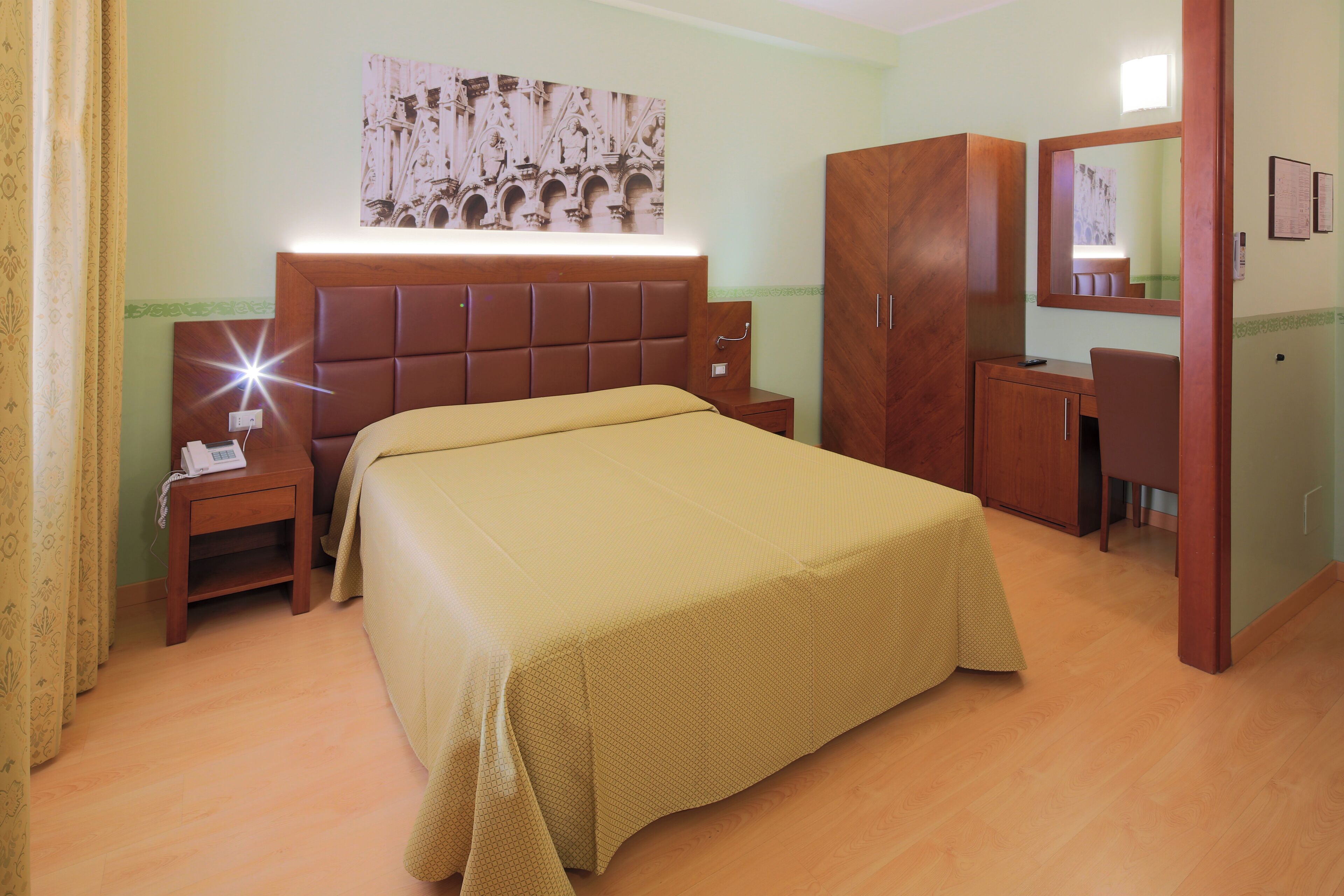 A hotel room with a bed, bedside table, nightstand, wardrobe, and a mirror.