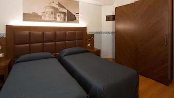 Una camera d'albergo con due letti singoli, un armadio in legno, un comodino e una lampada a parete.