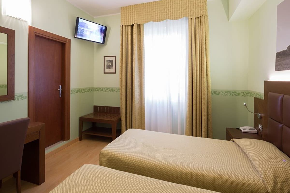 Ein Hotelzimmer mit zwei Betten, einem Fernseher, einem Schreibtisch und einem Stuhl.