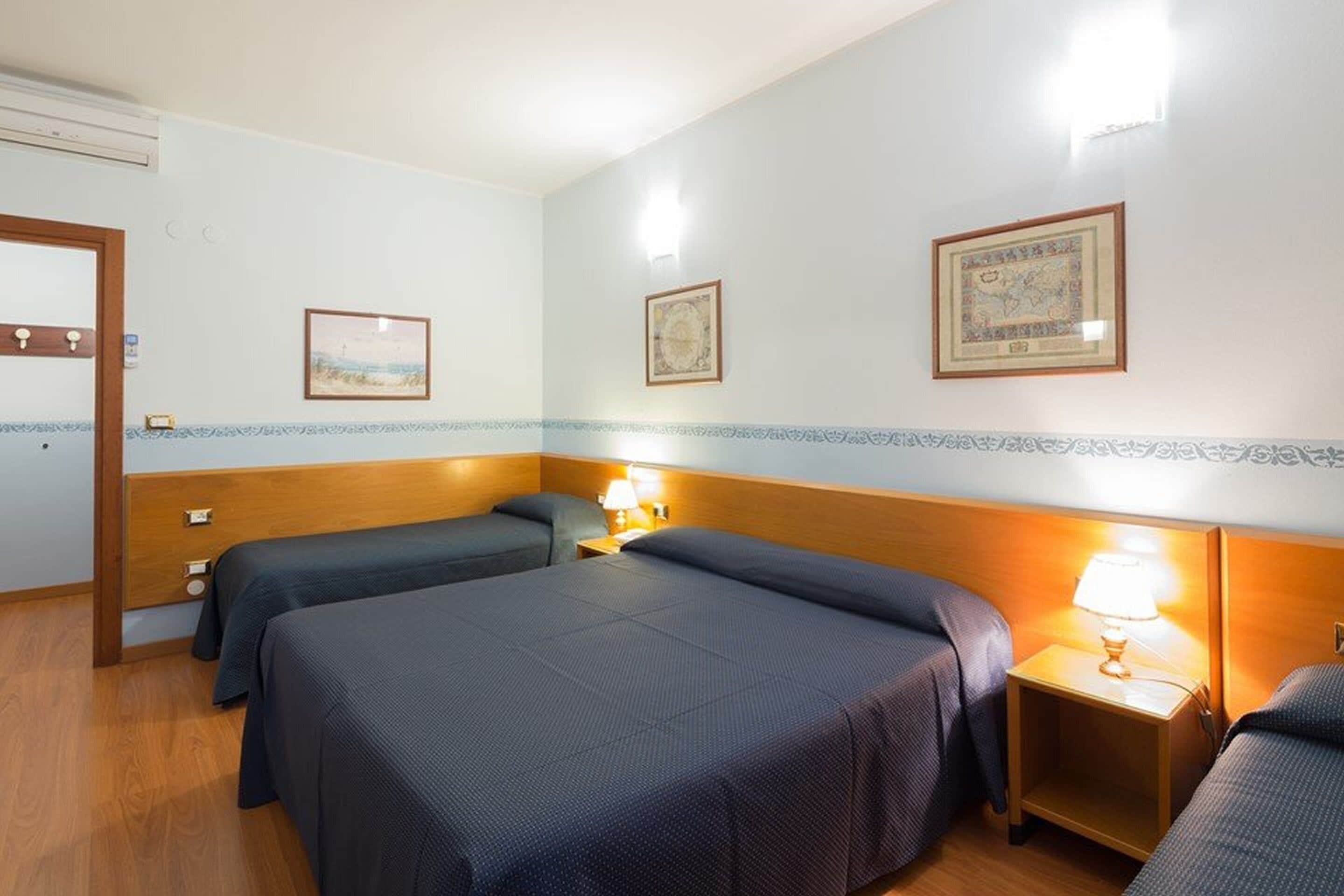 A hotel room with two beds, a wooden headboard, a nightstand with a lamp, and framed artwork on the wall.