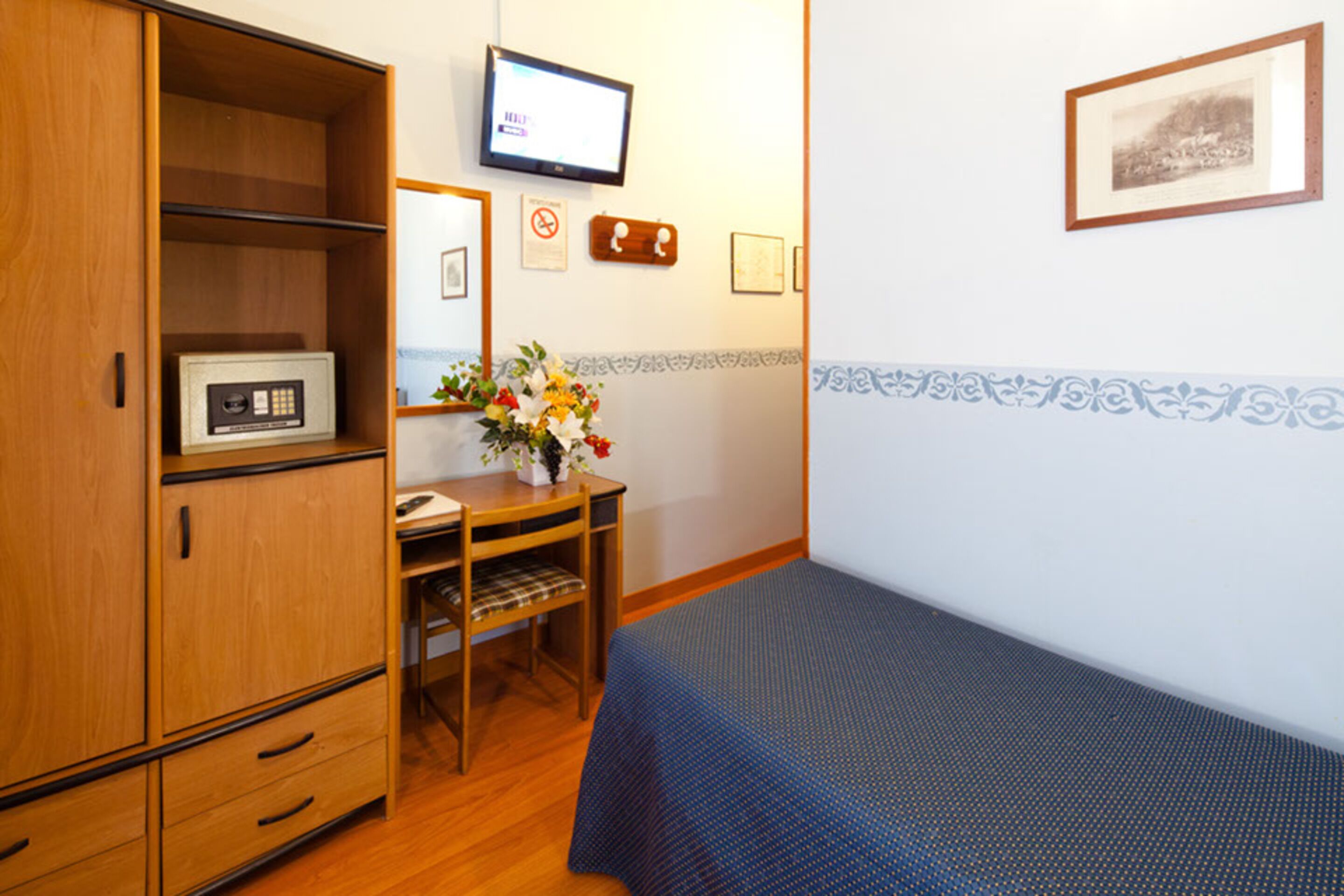 Ein Zimmer mit einem Bett, einem Holzschrank, einem Schreibtisch, einem Stuhl, einem Fernseher und einer Wand mit gerahmten Bildern.