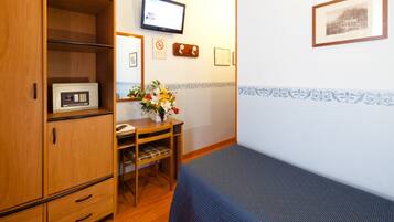 Ein Zimmer mit einem Bett, einem Holzschrank, einem Schreibtisch, einem Stuhl, einem Fernseher und einer Wand mit gerahmten Bildern.