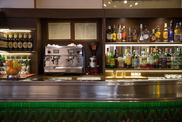 Una zona de bar con una máquina de café, estantes llenos de botellas de licores y una pizarra de menú.