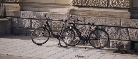 A bicycle parked against a stone building with a window and a metal railing.