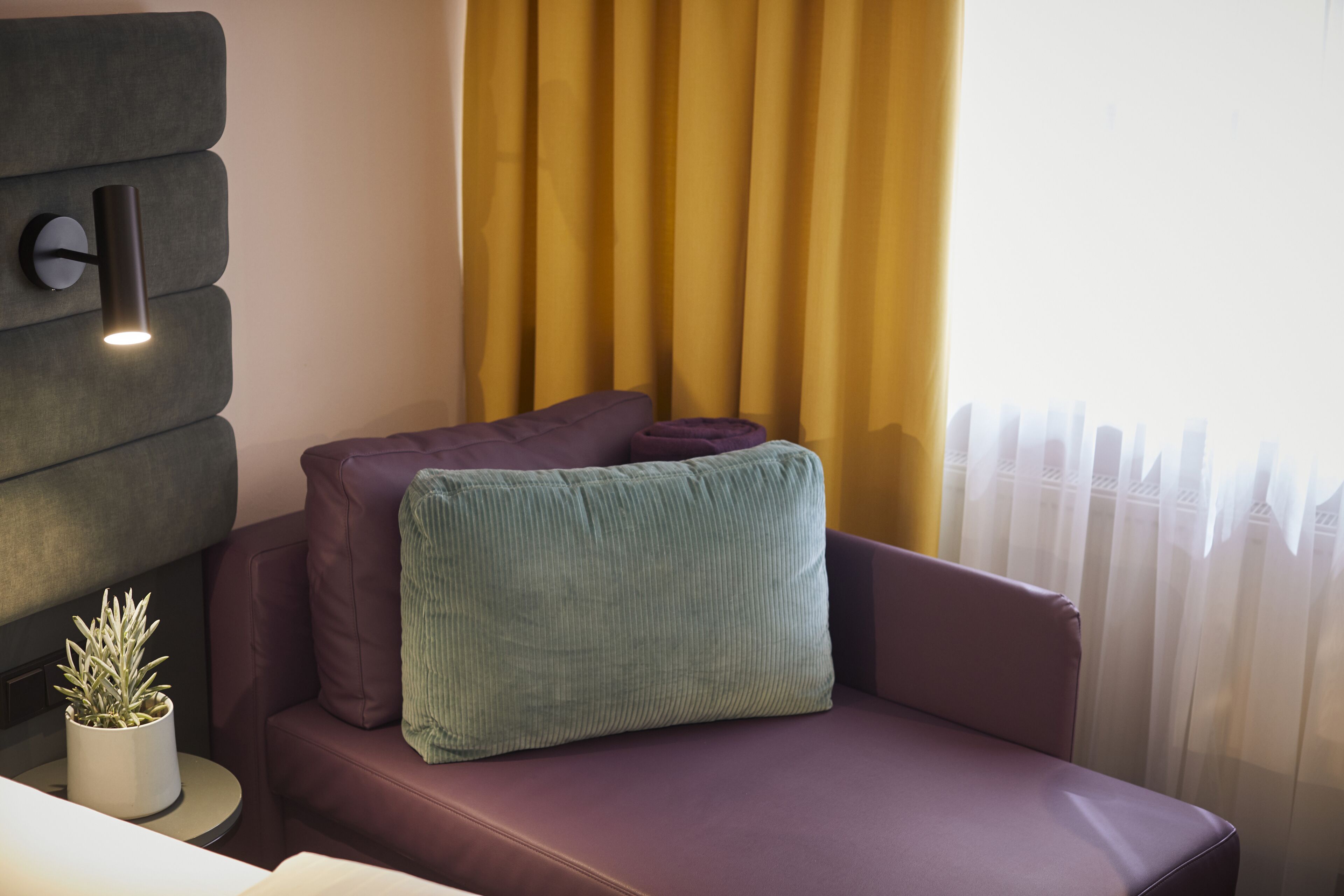 A modern room with a sofa, a small table with a plant, and a wall-mounted light fixture.