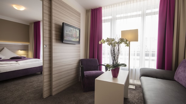 Une chambre d’hôtel avec un lit, une chaise, un canapé, un bureau, une lampe et une fenêtre avec des rideaux.