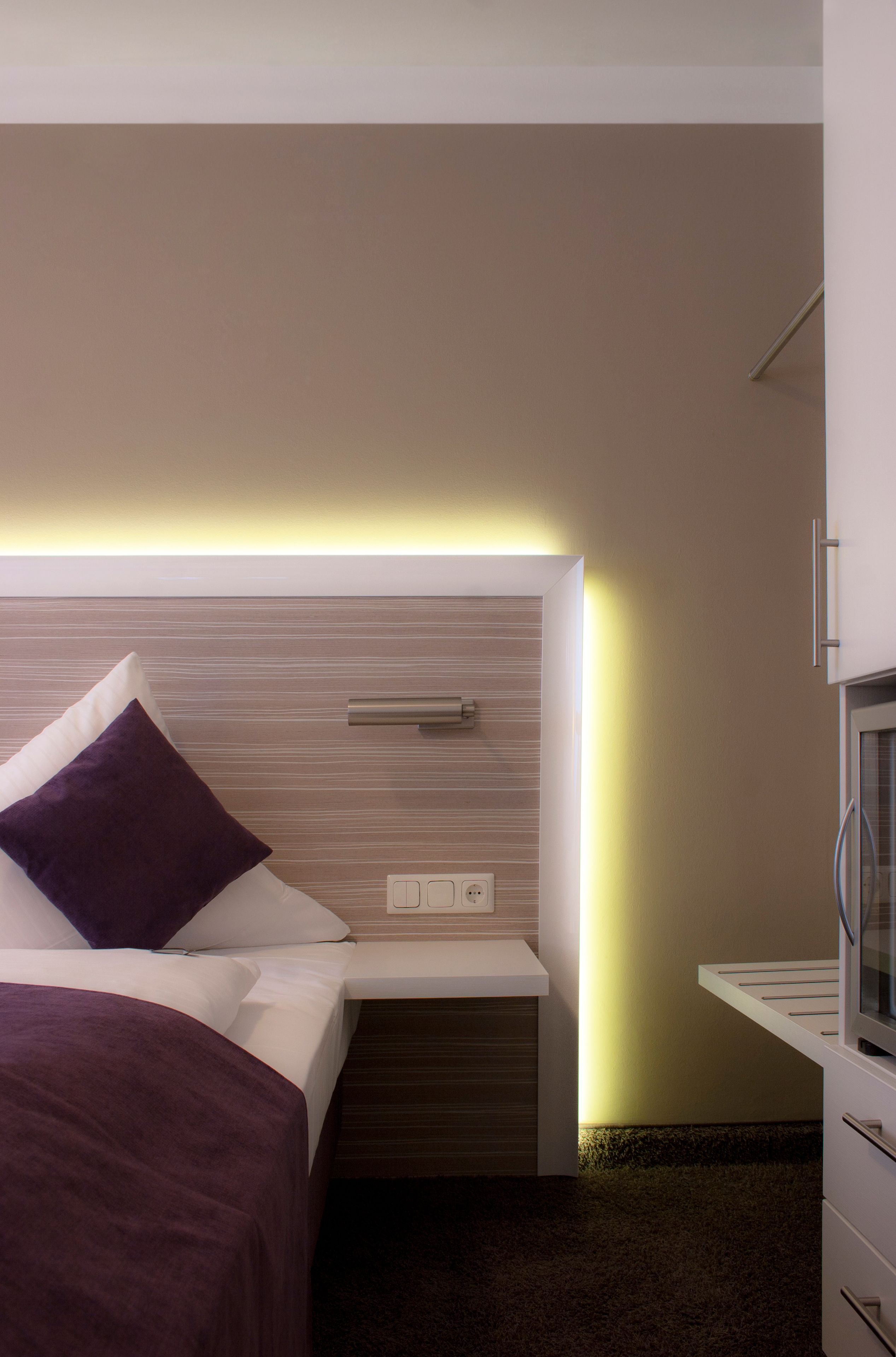 A modern hotel room with a neatly made bed, a bedside table, and a built-in TV.