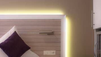 A modern hotel room with a neatly made bed, a bedside table, and a built-in TV.