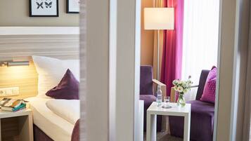 A hotel room with a bed, bedside table, a small table with a vase of flowers, and a sofa.