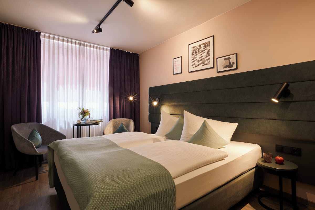 Camera d'albergo con due letti, una sedia, un tavolino e un comodino.