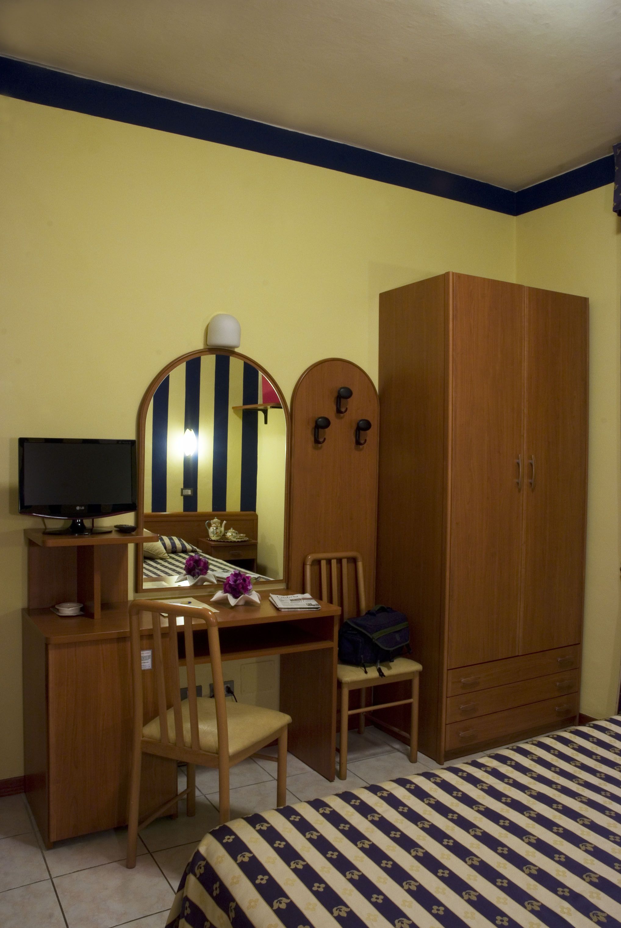 Une chambre à coucher comprenant un lit, un bureau avec une chaise, une télévision, une armoire et un miroir.