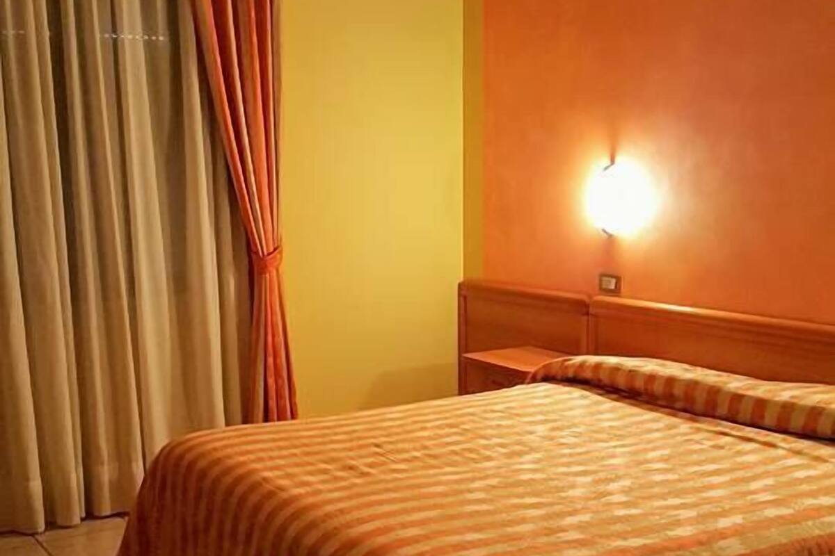 A hotel room with a bed, curtains, a wall-mounted light, and a tiled floor.