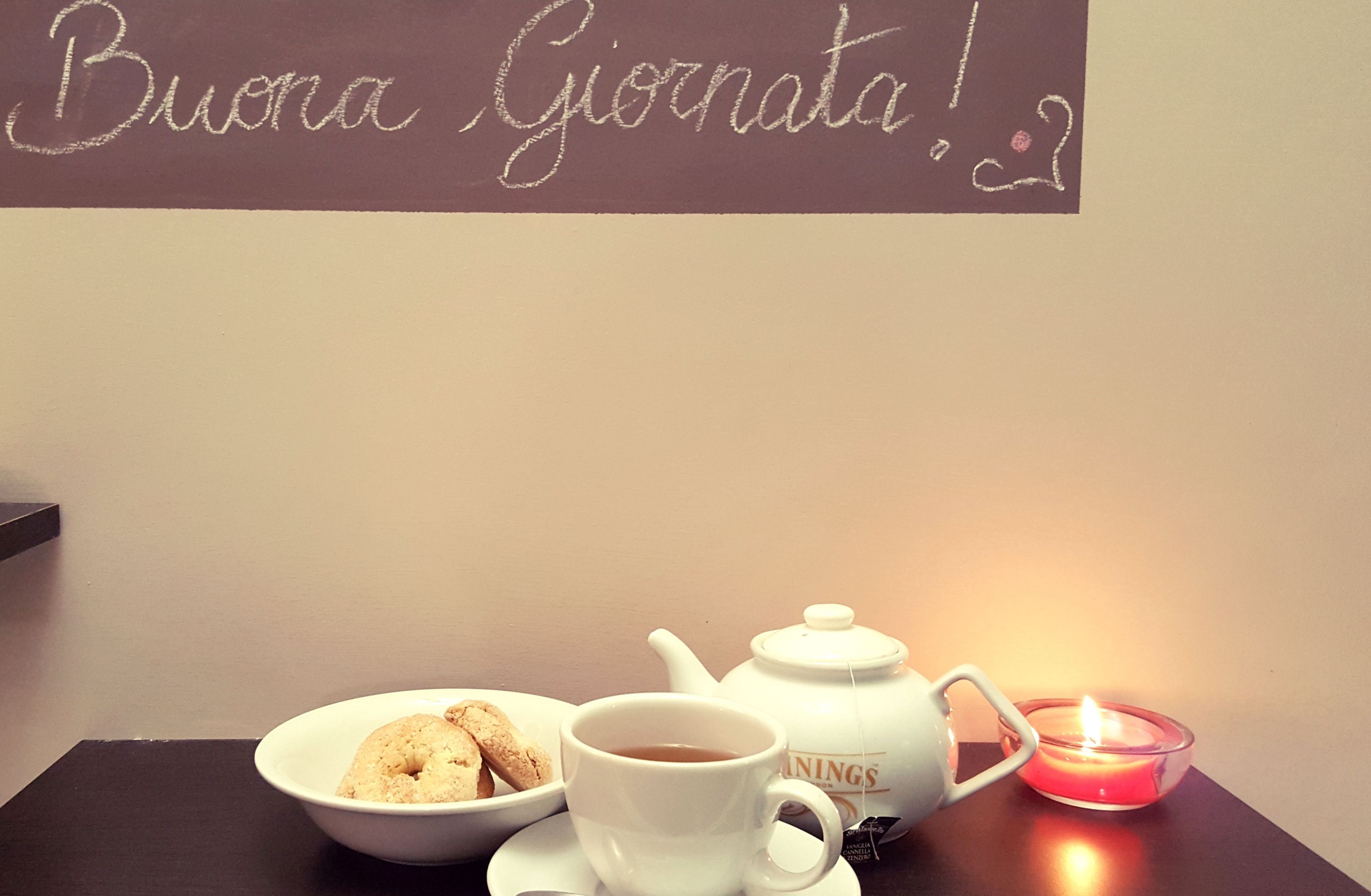A table with a teapot, cup, and bowl of cookies, and a candle.