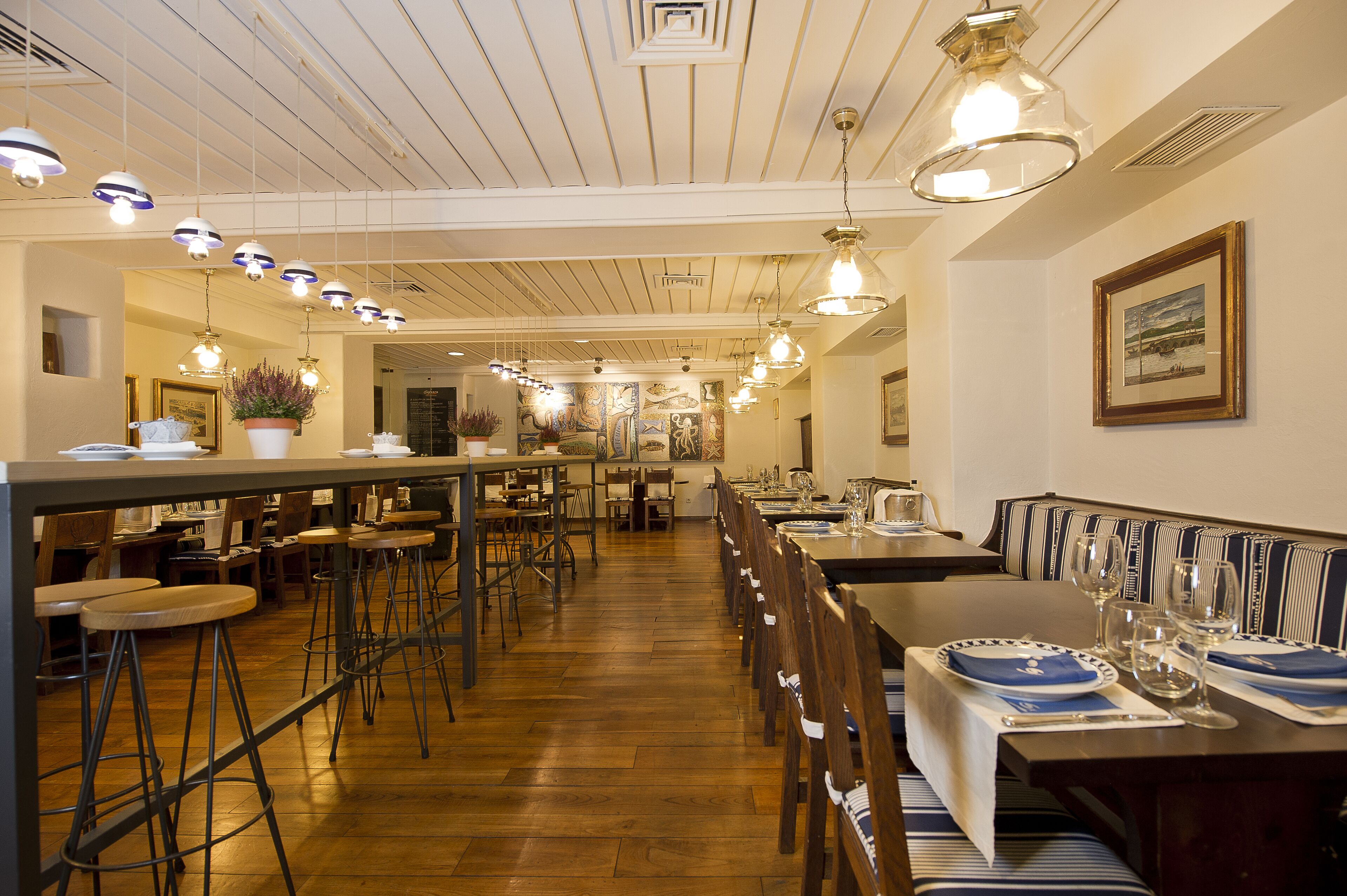 A restaurant with wooden floors, striped booths, and hanging pendant lights.