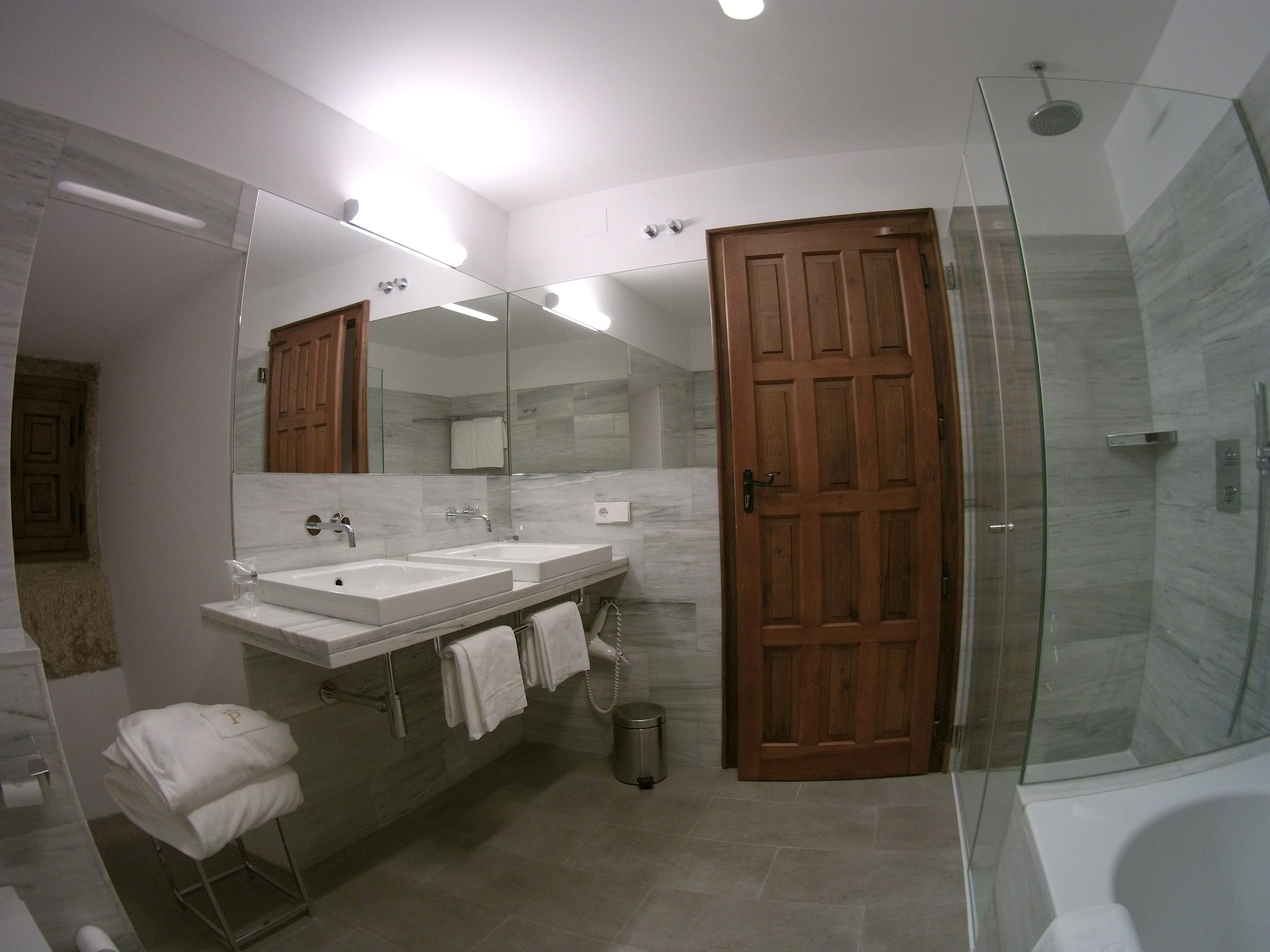 Un baño moderno con dos lavamanos, un espejo grande, una puerta de madera y una zona de ducha con mampara de cristal.