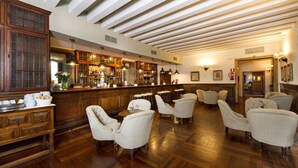 A bar area with wooden furniture, a bar counter, and a seating area with upholstered chairs. - Parador de Santiago de Compostela (Santiago de Compostela)