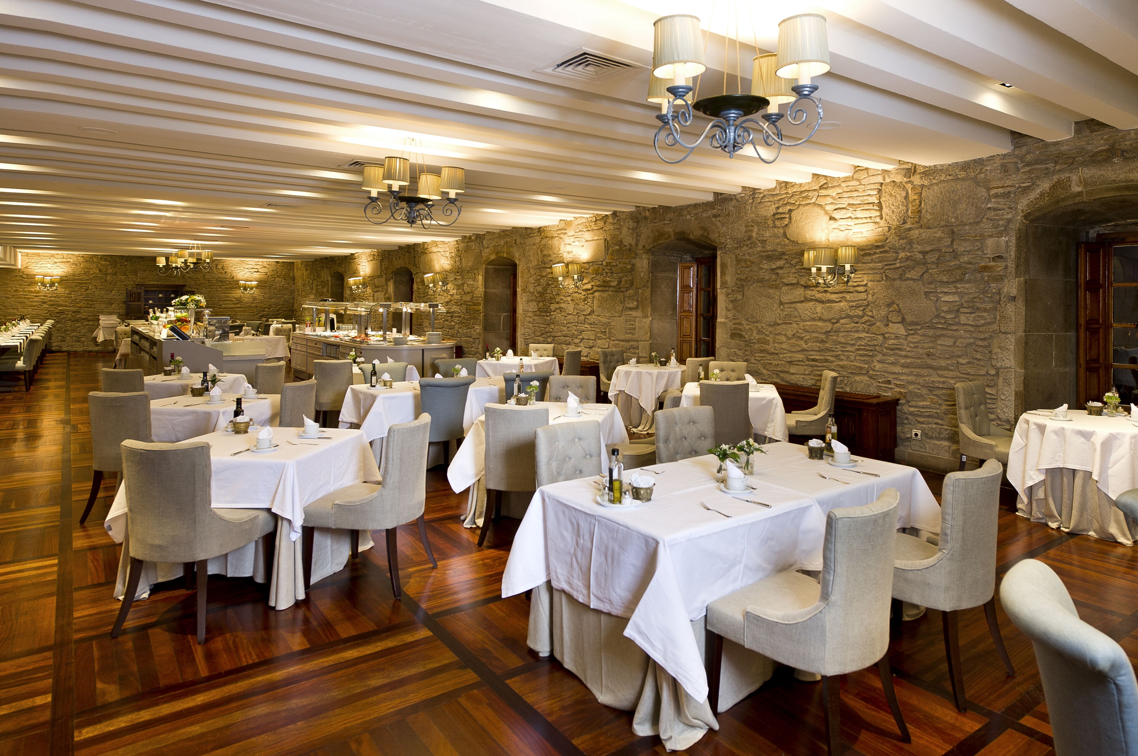 Ein geräumiger Essbereich mit mehreren gedeckten Tischen, gestaltet mit einer Steinwand und eleganten Kronleuchtern.