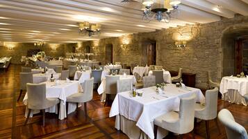 Un comedor amplio con varias mesas dispuestas para los comensales, que cuenta con un fondo de pared de piedra y elegantes candelabros.