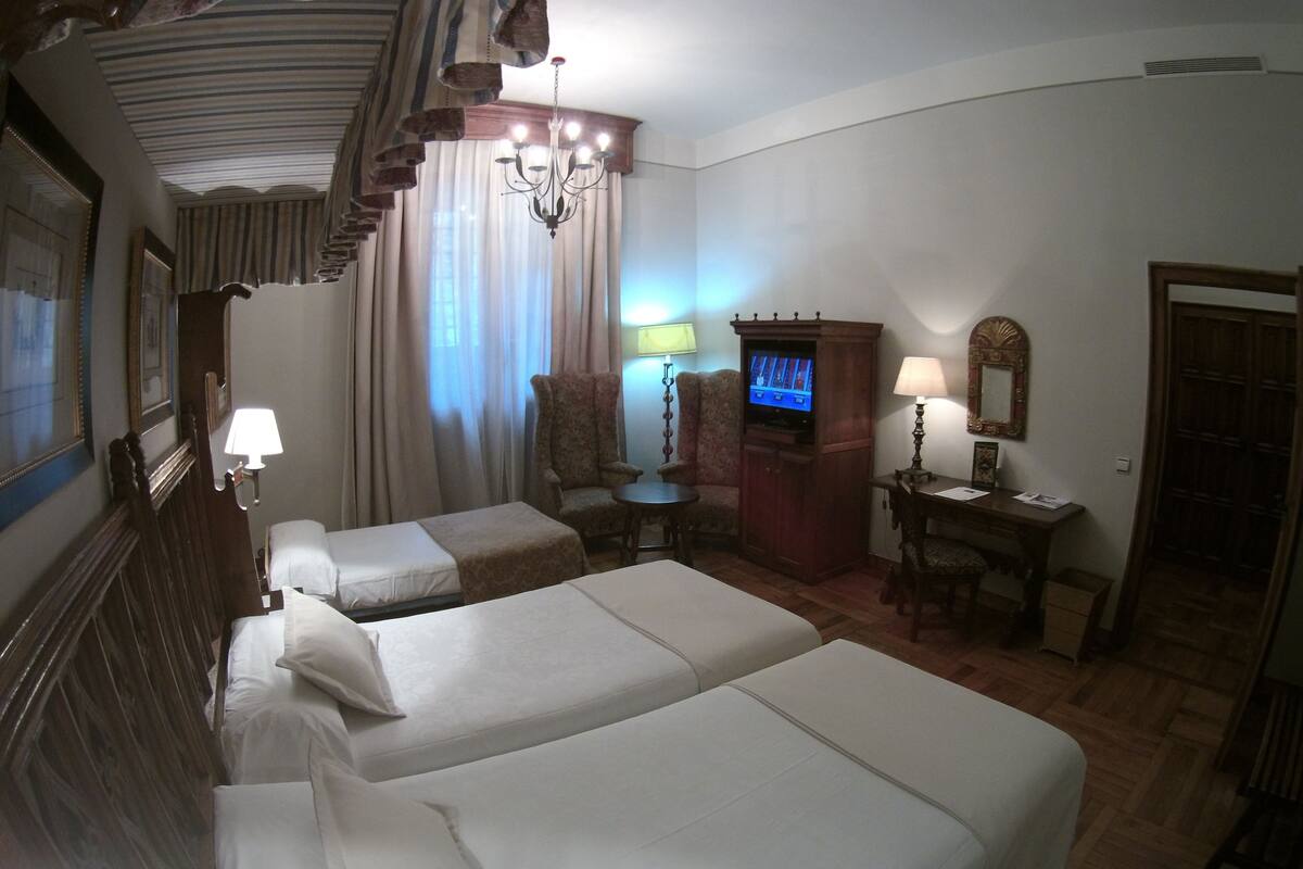 Ein Hotelzimmer mit zwei Betten, einem Schreibtisch mit Lampe, einem Fernseher und einem Sessel.