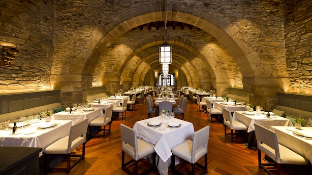 A long dining hall with stone walls and wooden beams, tables set for dining with chairs. - Parador de Santiago de Compostela (Santiago de Compostela)