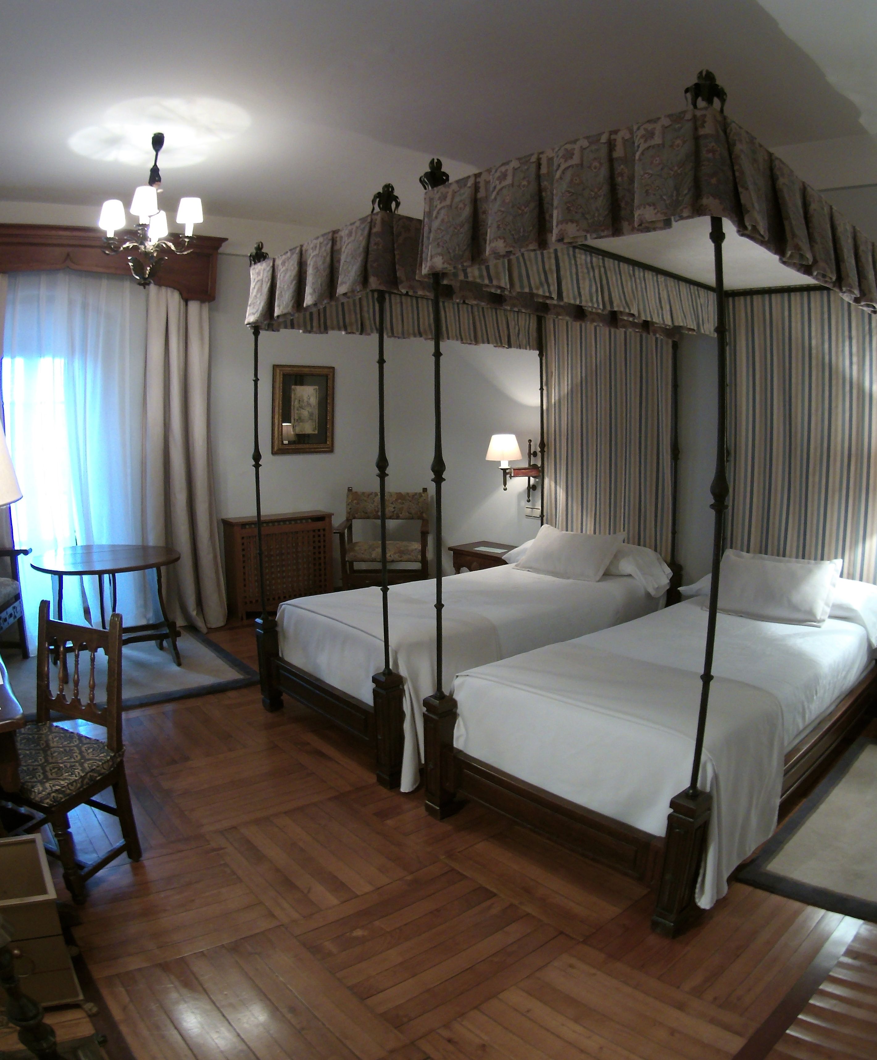 Un lit à baldaquin à quatre poteaux avec deux lits, un plancher en bois, une chaise, une table et une lampe.