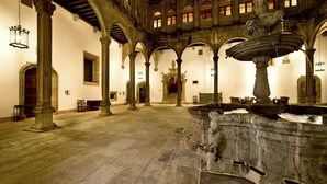 An interior with stone columns, a fountain, and a staircase leading to an upper level. - Parador de Santiago de Compostela (Santiago de Compostela)