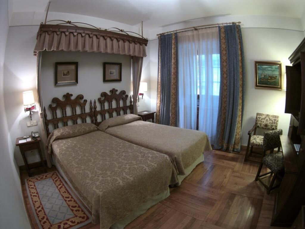 Una cama doble con cabecera, una mesita de noche, una silla, un escritorio y una ventana con cortinas.
