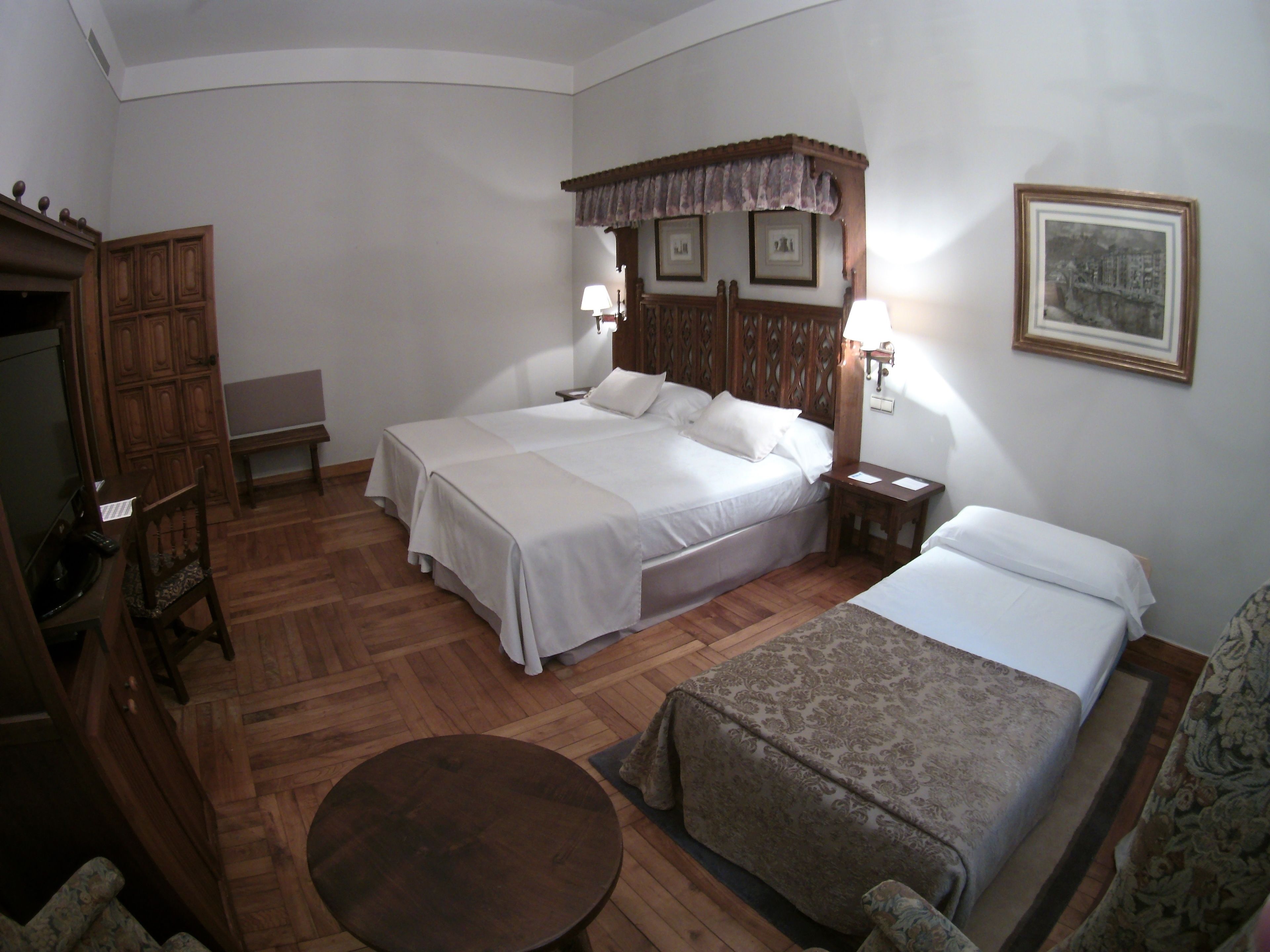 A hotel room with two beds, a wooden headboard, a small table, and a television.
