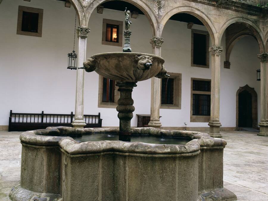 Ein Innenhof mit einem Steinfountain, gewölbten Gängen und einer Bank.