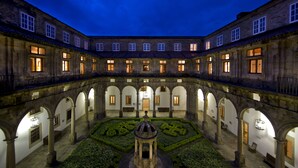 A courtyard with a central fountain, surrounded by arches and buildings with illuminated windows. - Parador de Santiago de Compostela (Santiago de Compostela)