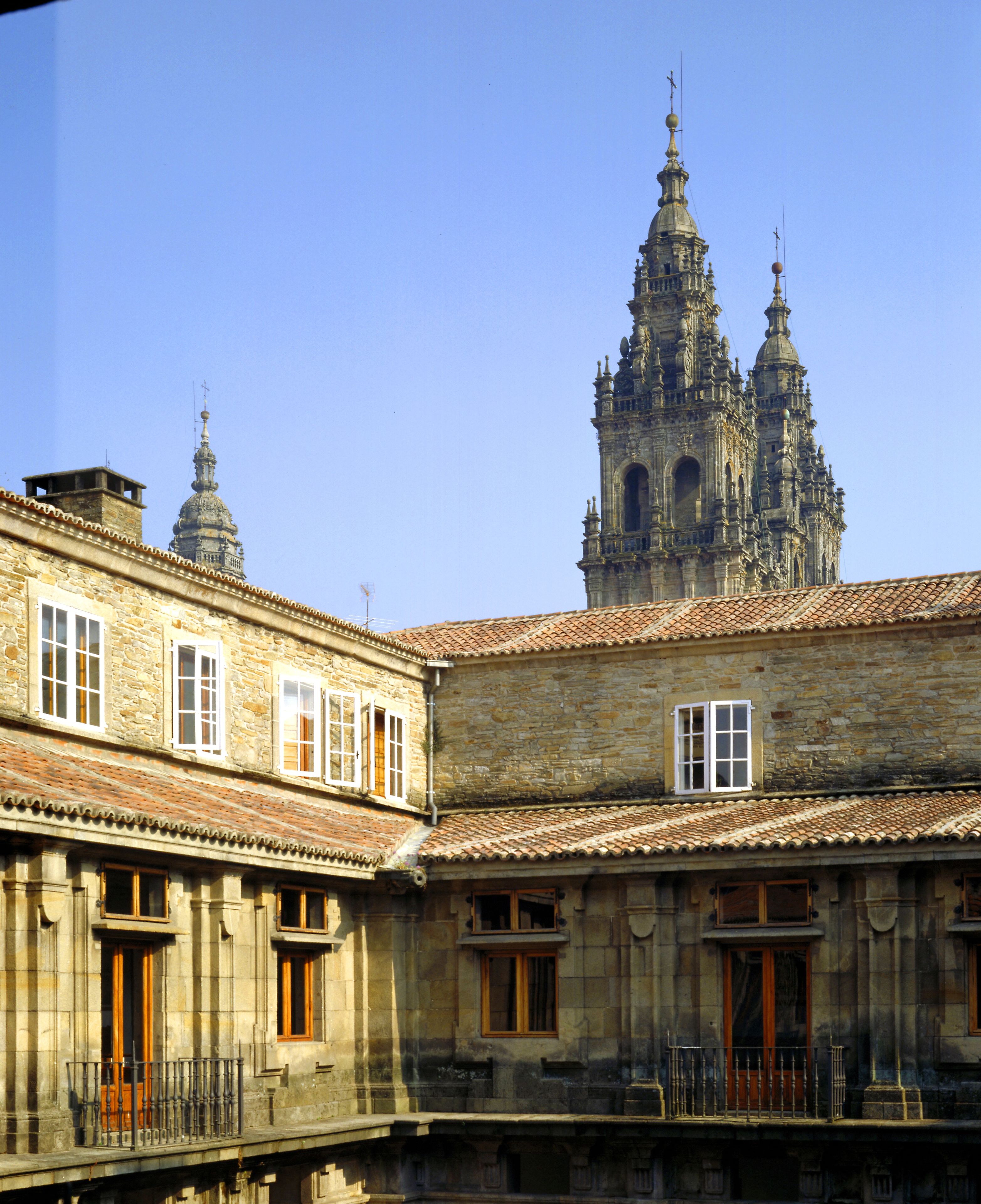A historic building with a courtyard, stone facade, and a prominent church tower in the background.
