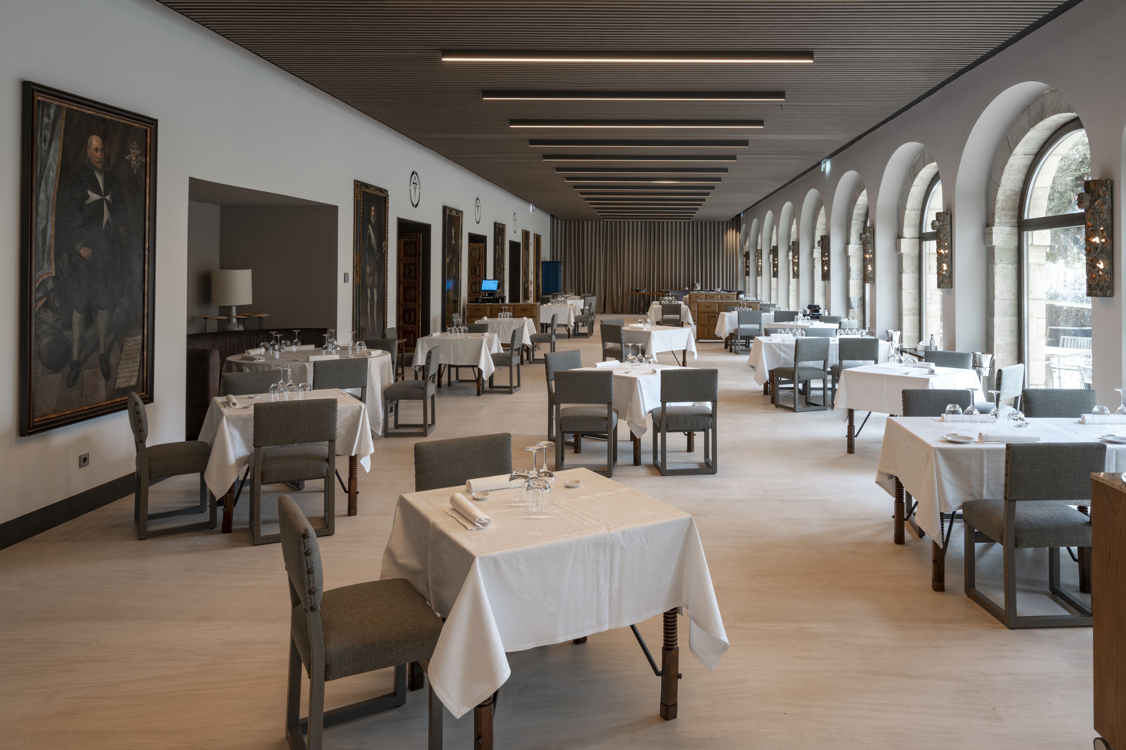 Un comedor amplio con varias mesas y sillas, ventanas grandes y un diseño moderno en el techo.