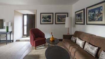 Una sala de estar con un sillón rojo, un sofá marrón, una mesa de centro negra y una lámpara. Hay tres cuadros enmarcados en la pared.