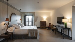 Quarto de hotel com cama, escrivaninha, cadeira, televisão e luminária.