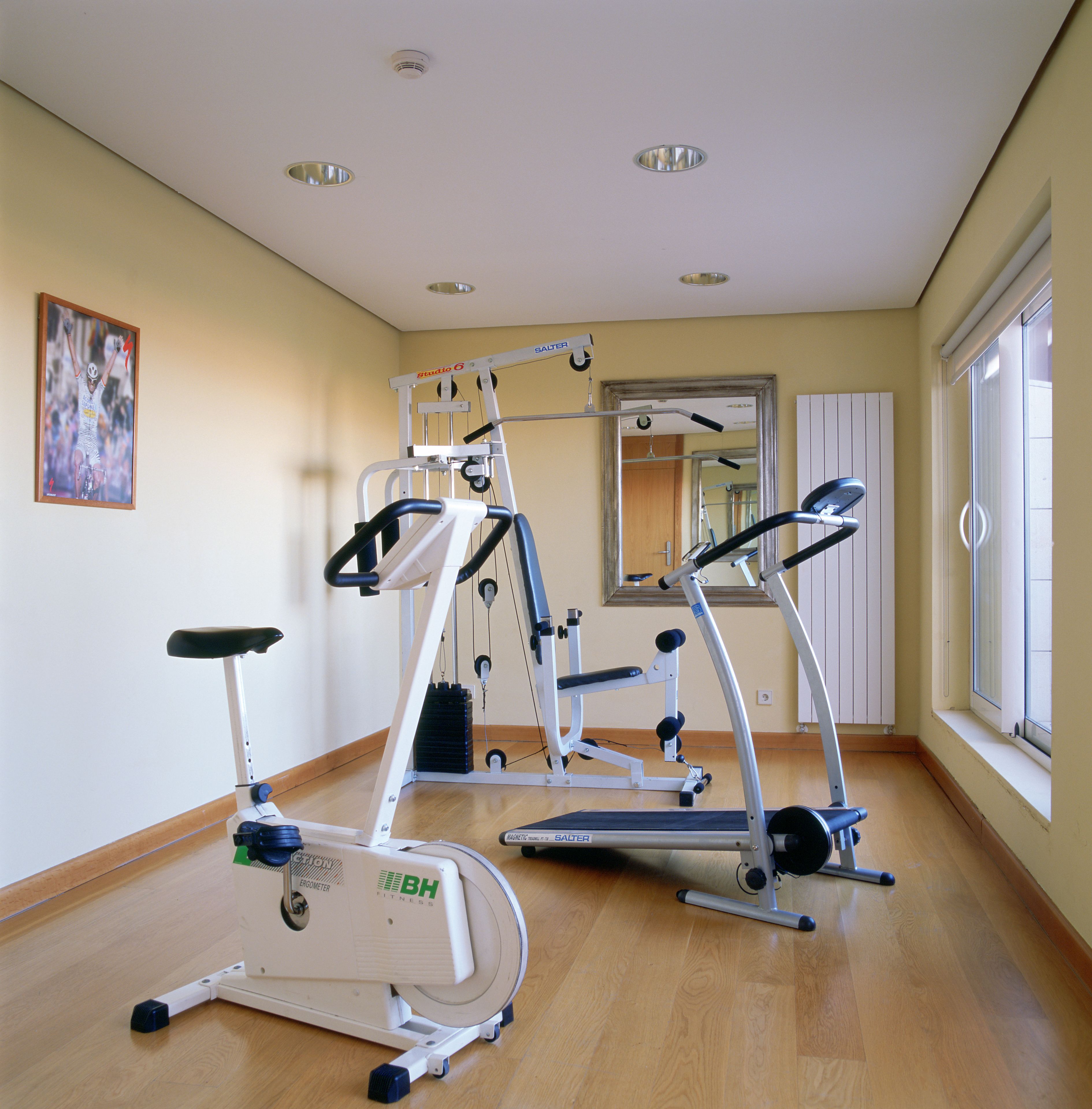A gym with exercise equipment, a mirror, and a window with blinds.