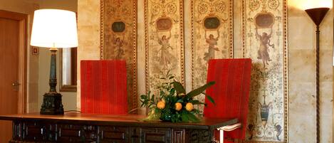 A room with a wooden table, red chairs, a red rug, and a wall with ornate floral patterns.